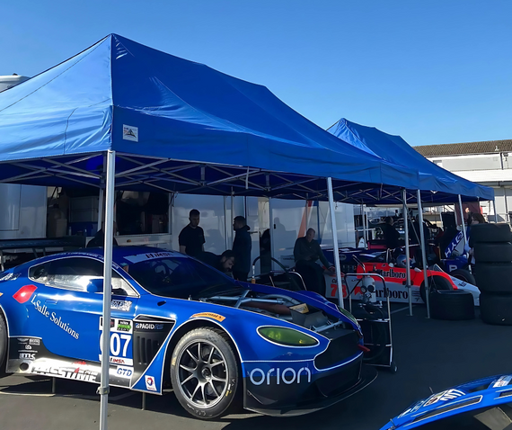 gala performance blue race car under blue pit gazebo trackside